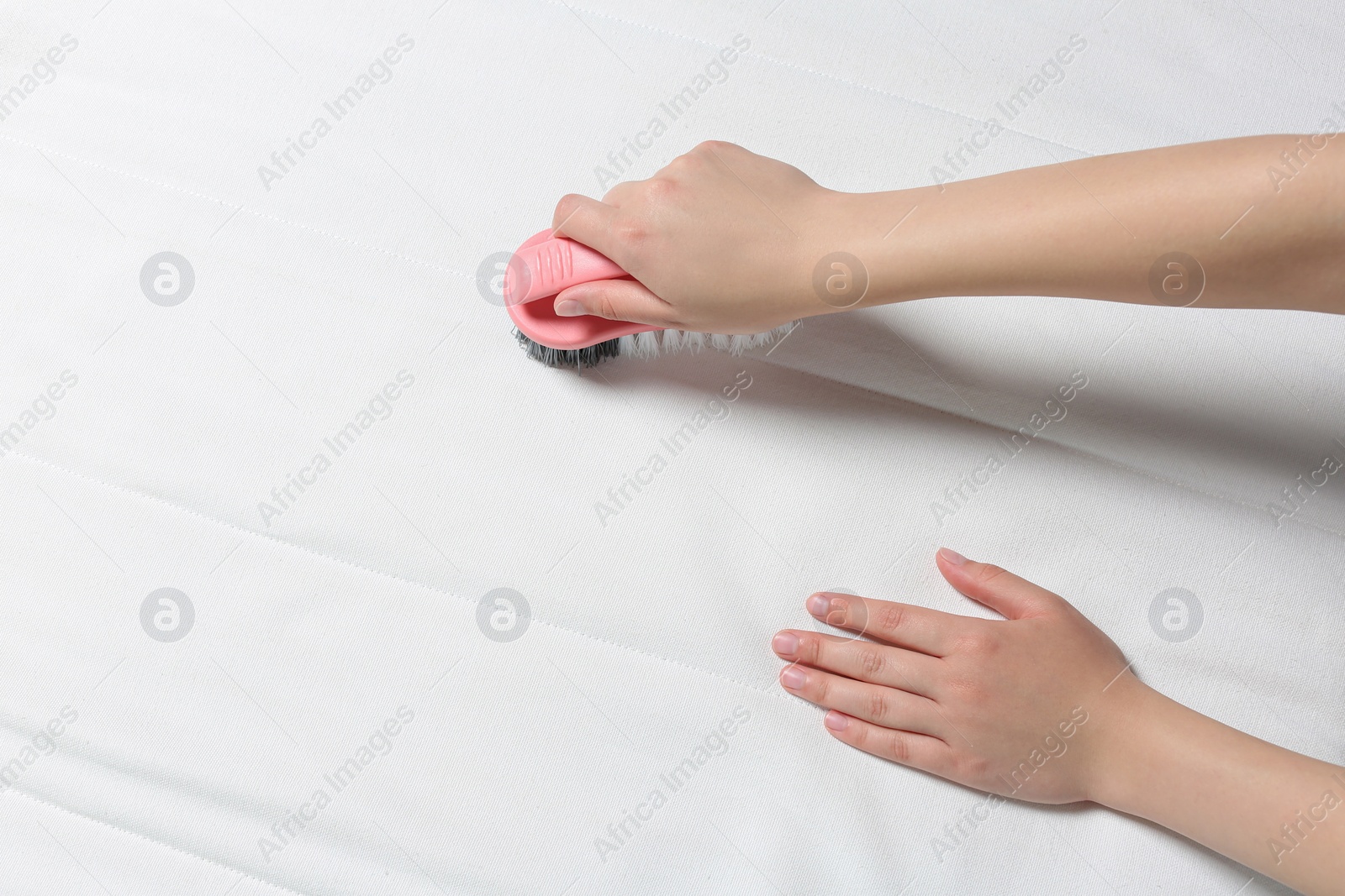 Photo of Woman cleaning white mattress with brush, closeup. Space for text