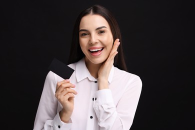 Photo of Happy woman holding blank business card on black background