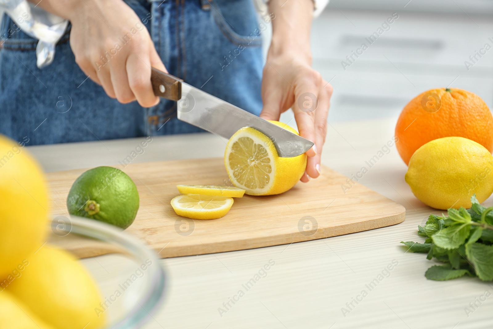Photo of Woman cutting fruit for making natural detox lemonade at table in kitchen, closeup