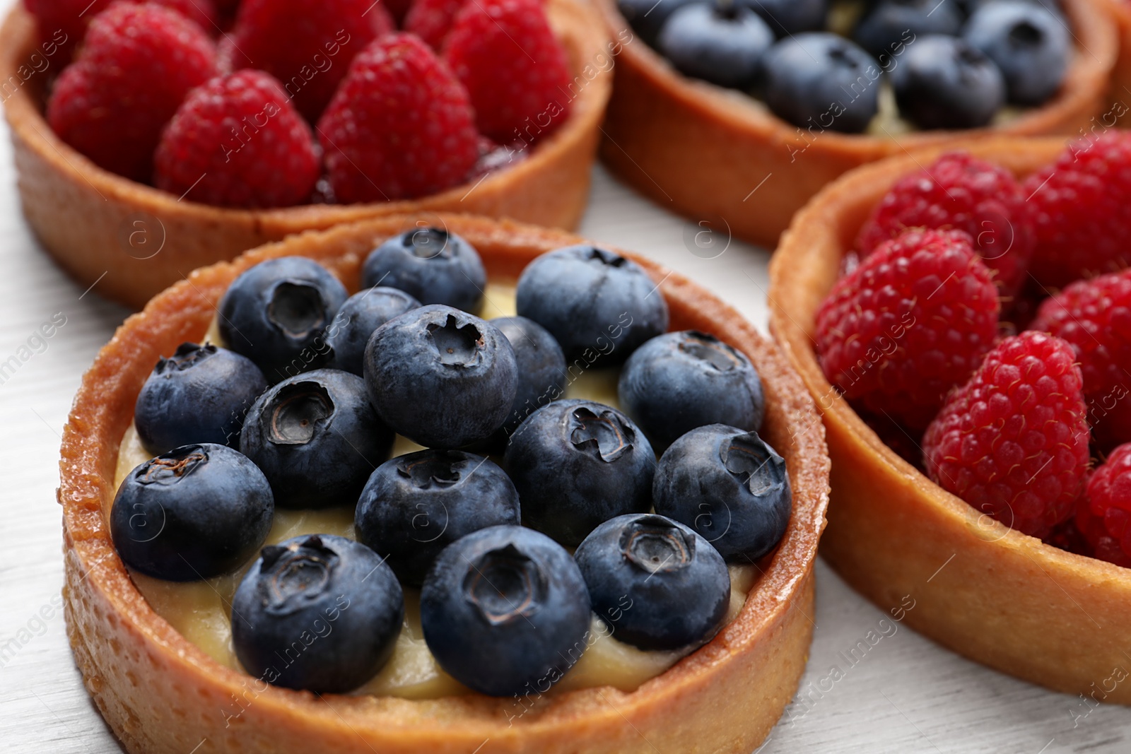 Photo of Tartlets with different fresh berries on white table, closeup. Delicious dessert