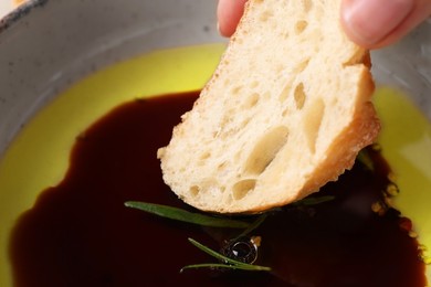 Photo of Woman dipping piece of bread into balsamic vinegar with oil and rosemary in bowl closeup