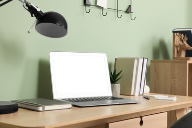 Image of Comfortable workplace at home. Modern laptop with blank screen and lamp on wooden desk. Mockup for design