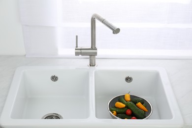Modern sink with water tap and fresh vegetables near window in kitchen