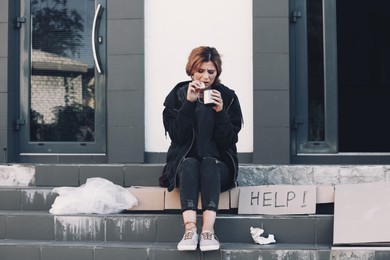 Image of Poor woman with piece of bread and mug on city street