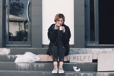 Poor woman with piece of bread and mug on city street