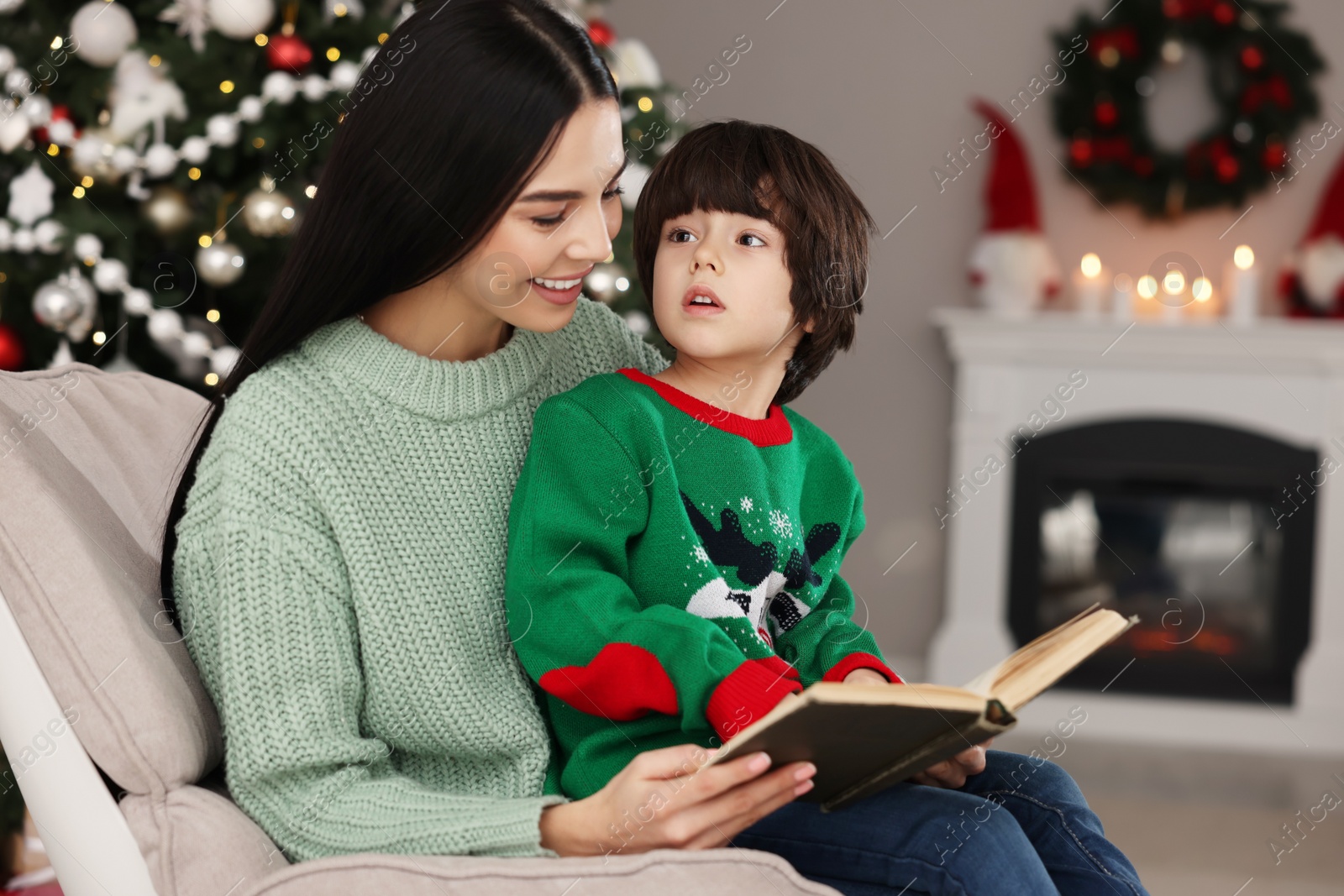 Photo of Mother with her cute son reading book in room decorated for Christmas