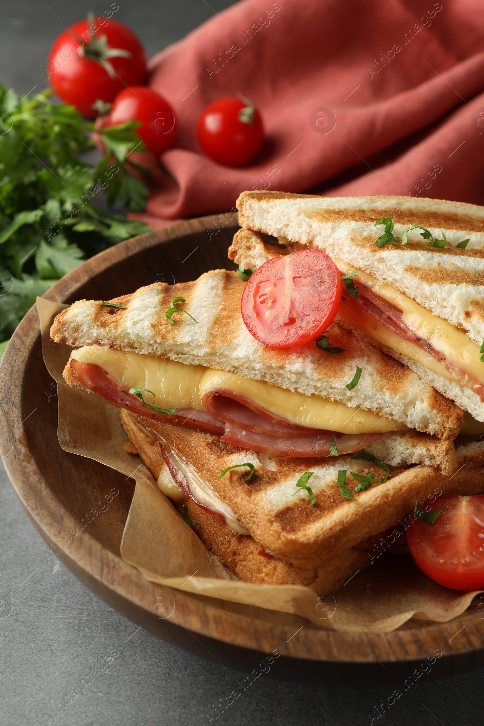 Photo of Tasty sandwiches with ham, tomato and melted cheese in bowl on grey table, closeup