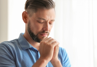 Photo of Man with hands clasped together for prayer on light background. Space for text