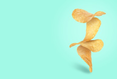 Tasty potato chips falling on turquoise background, space for text