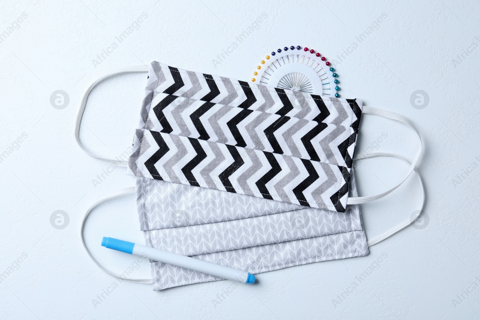 Photo of Homemade protective masks, pen and sewing pins on white background, flat lay
