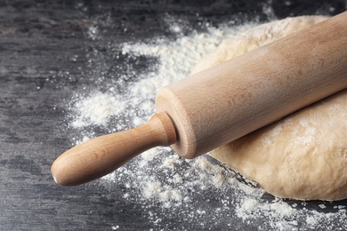 Photo of Raw wheat dough with flour and rolling pin on table, closeup