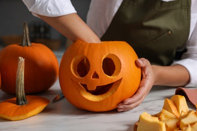 Woman carving pumpkin for Halloween at white marble table, closeup