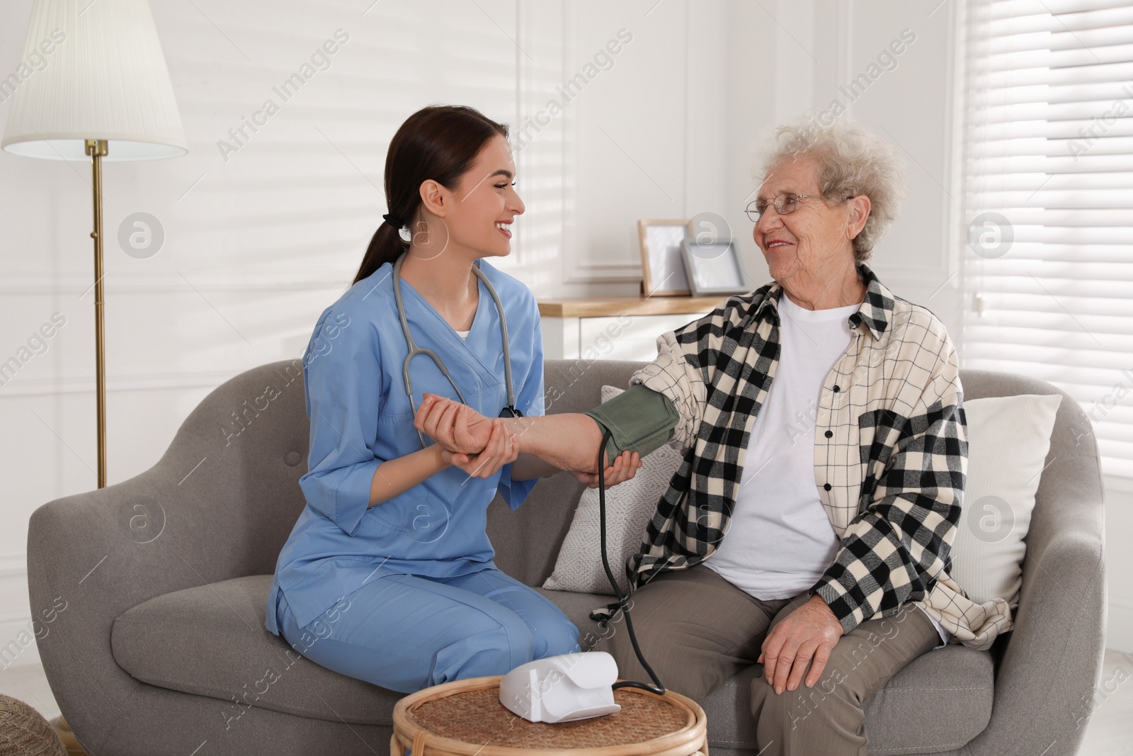 Photo of Young caregiver measuring blood pressure of senior woman in room. Home health care service