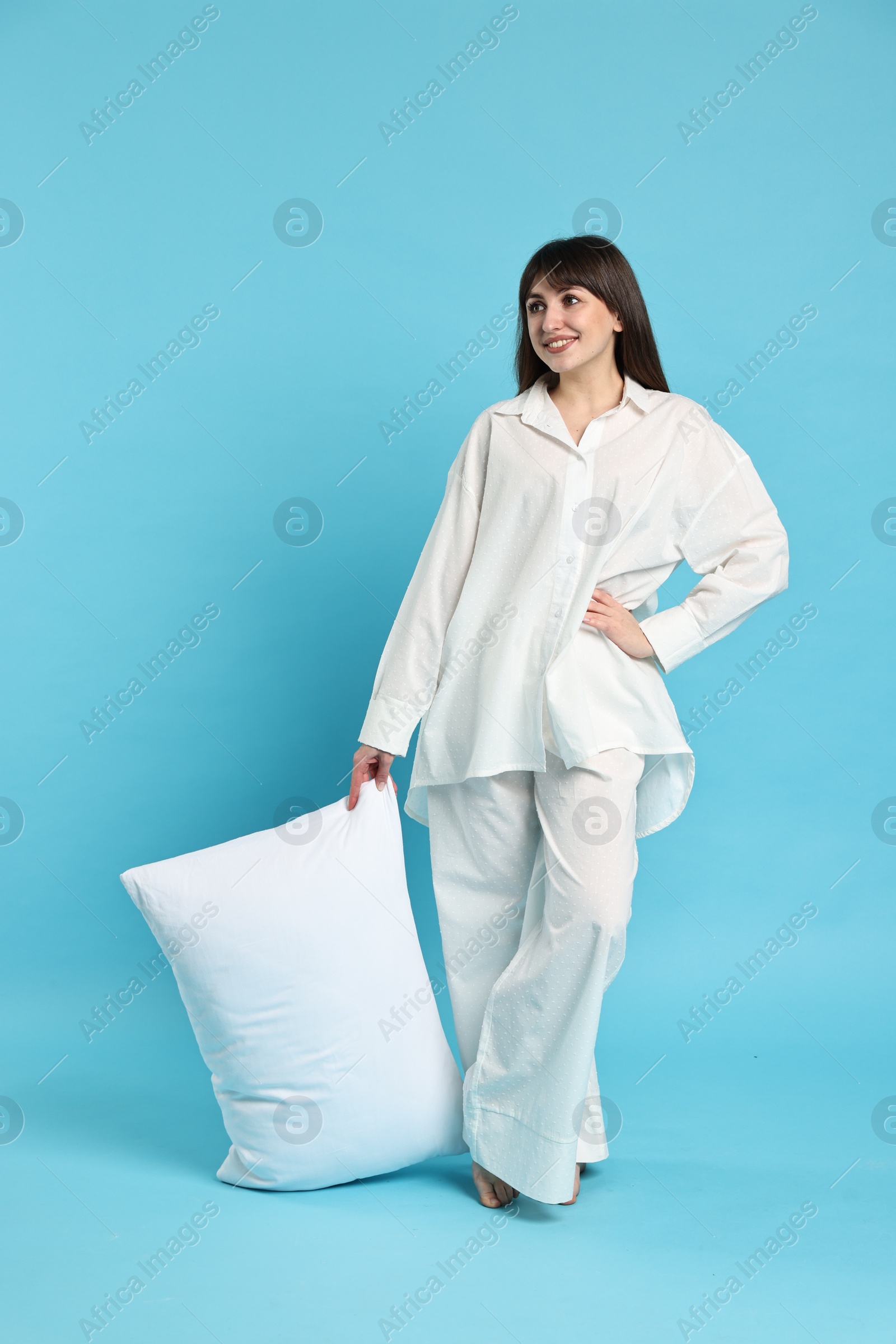 Photo of Happy woman in pyjama holding pillow on light blue background