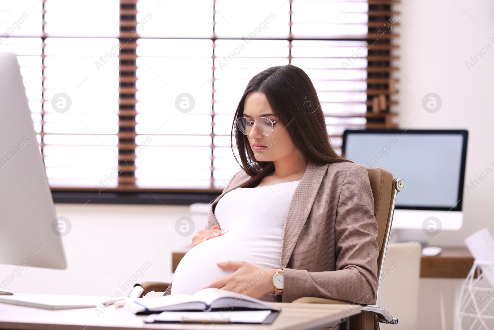 Photo of Young pregnant woman suffering from pain while working in office