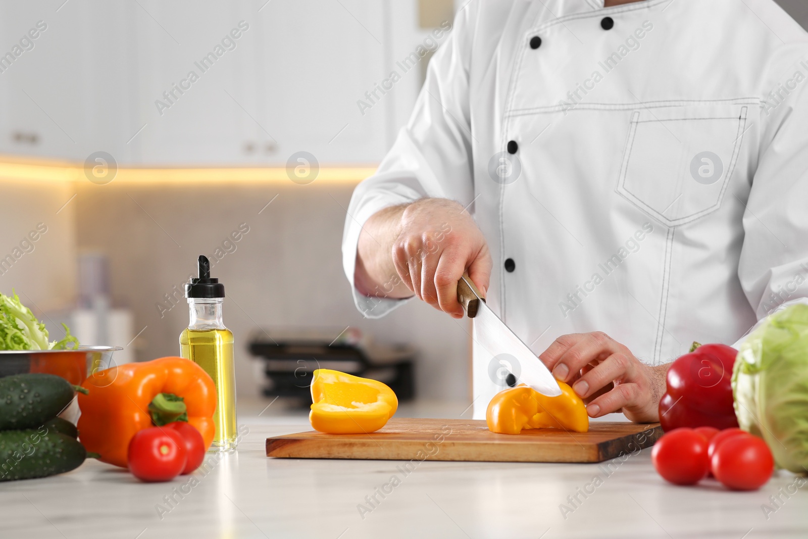 Photo of Chef cutting bell pepper at marble table in kitchen, closeup. Space for text