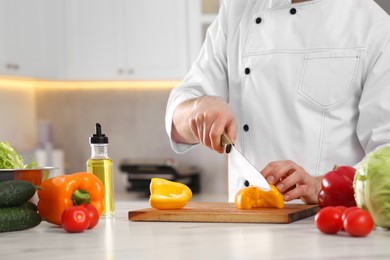 Photo of Chef cutting bell pepper at marble table in kitchen, closeup. Space for text