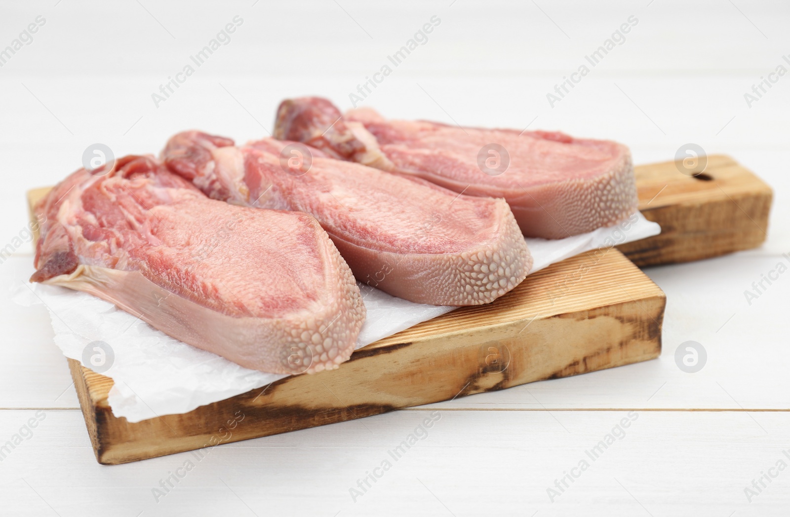 Photo of Raw beef tongue pieces on white wooden table, closeup