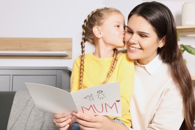 Photo of Happy woman receiving greeting card from her little daughter at home