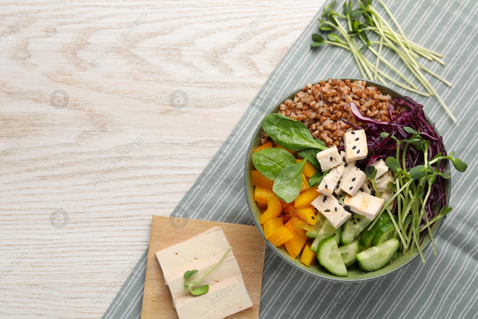 Photo of Delicious vegan bowl with bell pepper, tofu and buckwheat on wooden table, top view. Space for text