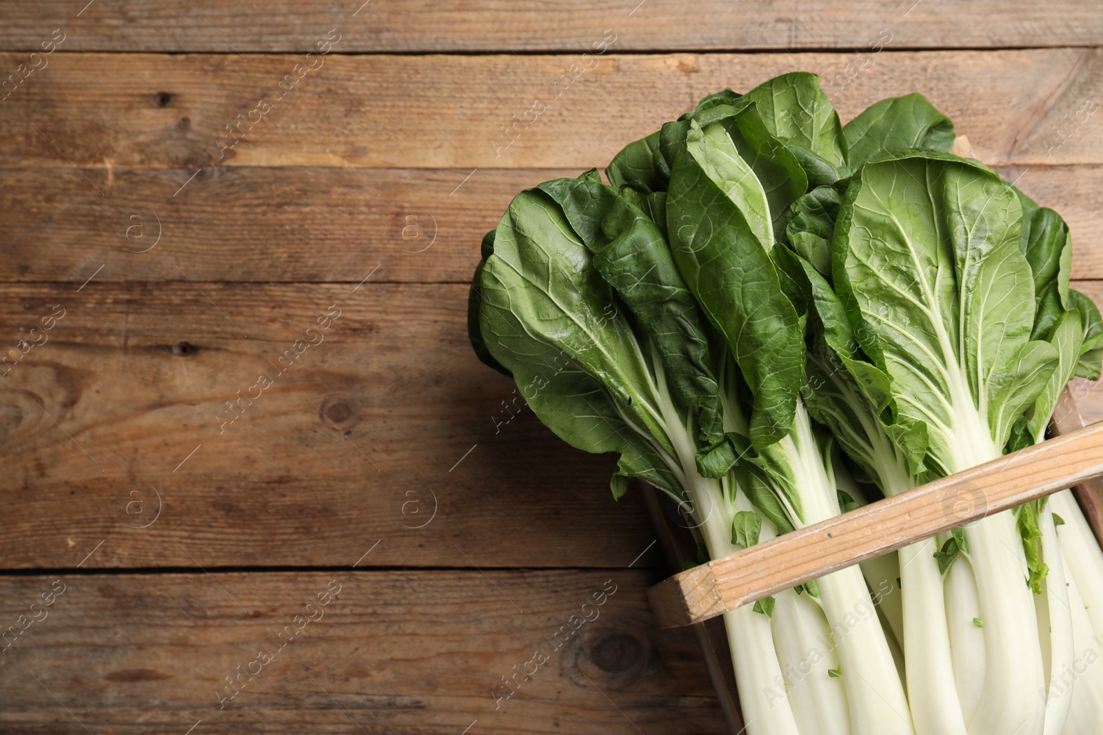 Photo of Fresh green pak choy cabbages in crate on wooden table, top view. Space for text