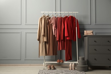 Rack with different stylish women`s clothes, shoes and bag on chest of drawers near grey wall indoors. Space for text
