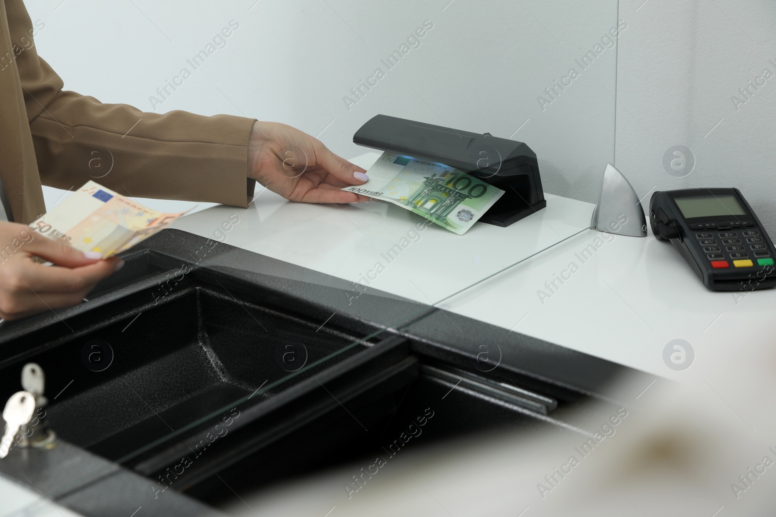 Photo of Cashier checking money with detector at currency exchange department in bank, closeup