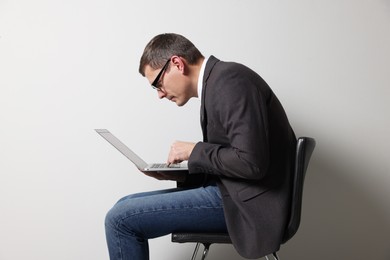 Photo of Man with bad posture using laptop while sitting on chair against grey background