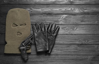 Photo of Beige knitted balaclava, gloves and gun on grey wooden table, flat lay. Space for text