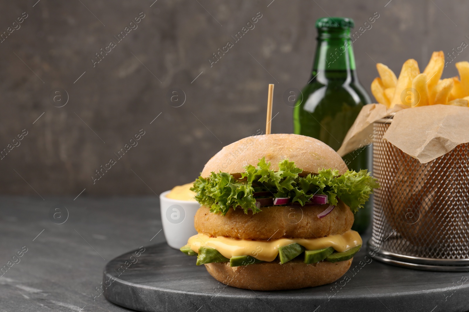 Photo of Tasty vegetarian burger served with french fries and beer on black table, space for text