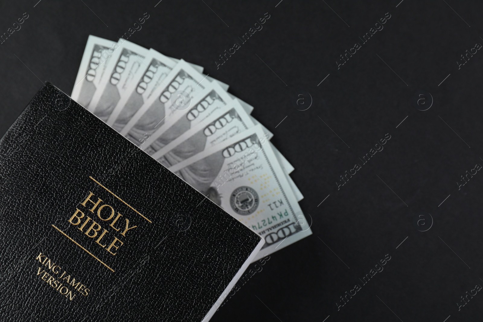 Photo of Holy Bible with money on black background, top view. Space for text