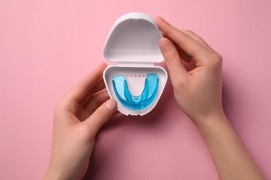 Woman holding container with mouth guard on light pink background, top view. Bite correction