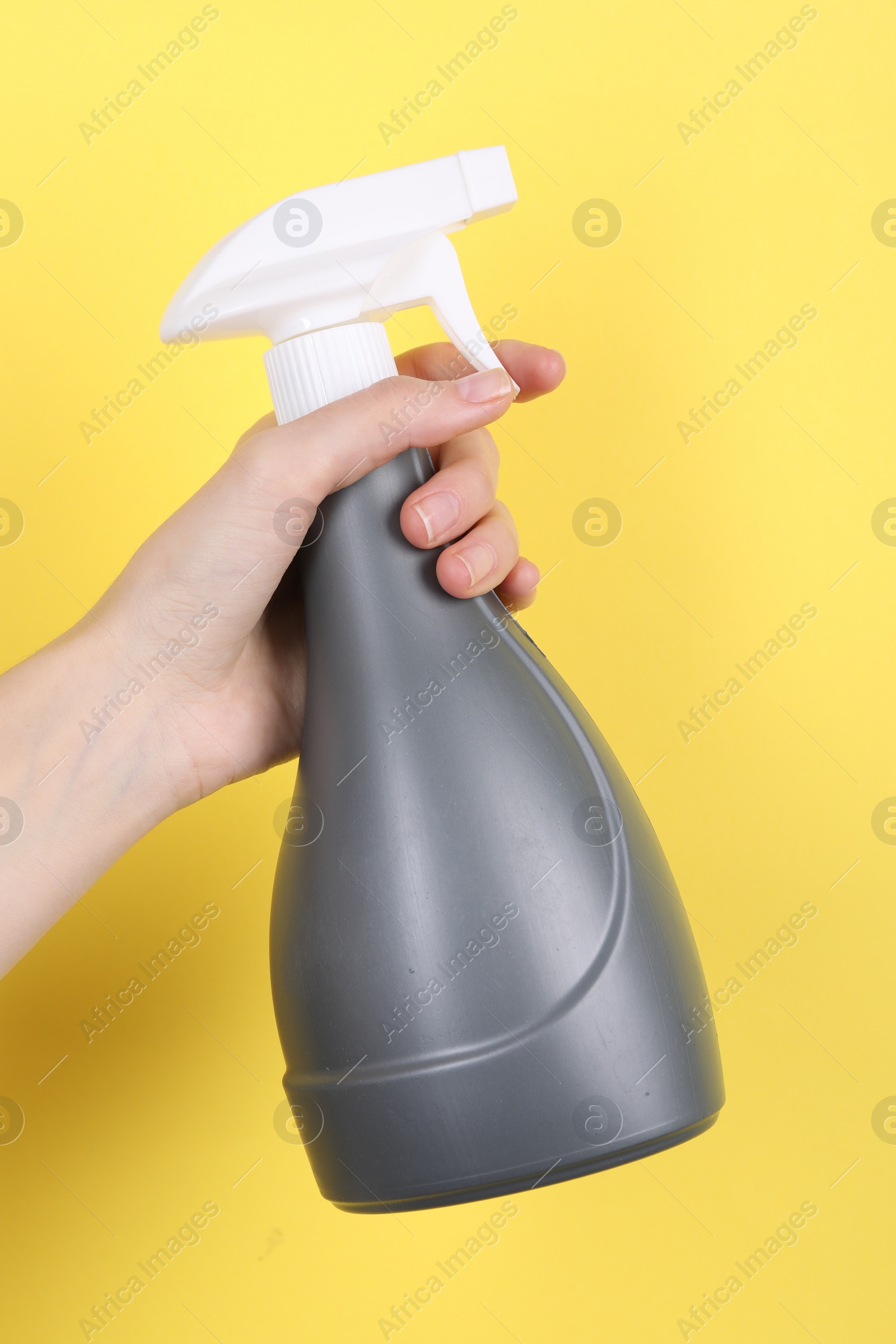 Photo of Woman holding plastic spray bottle on yellow background, closeup