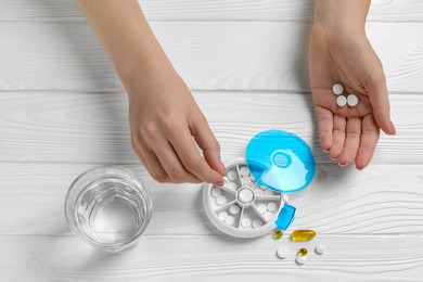 Woman putting pill into plastic box at white wooden table, top view