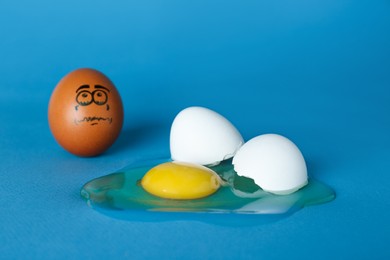 Photo of Whole egg with sad face and broken one on blue background