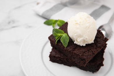 Photo of Tasty brownies served with ice cream and mint on white marble table, closeup. Space for text