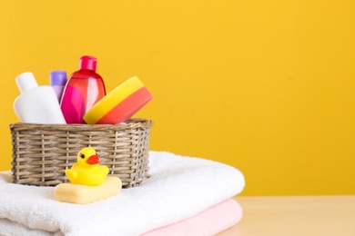 Photo of Wicker basket with baby cosmetic products, toy and towels on table against color background. Space for text