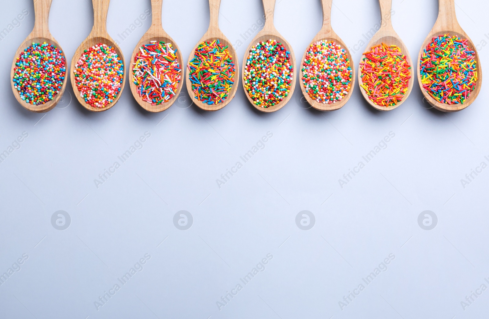 Photo of Colorful sprinkles in spoons on light grey background, flat lay with space for text. Confectionery decor