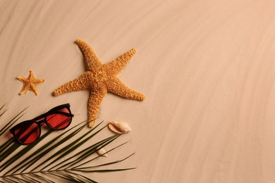 Photo of Flat lay composition with stylish sunglasses and starfishes on sand, space for text. Beach accessory