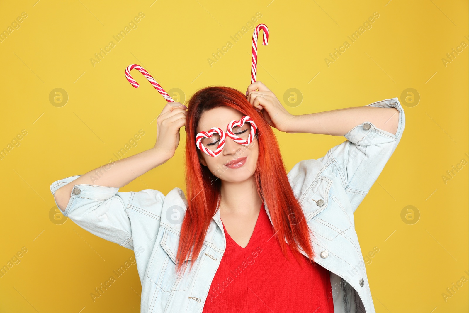 Photo of Young woman with bright dyed hair holding candy canes on yellow background