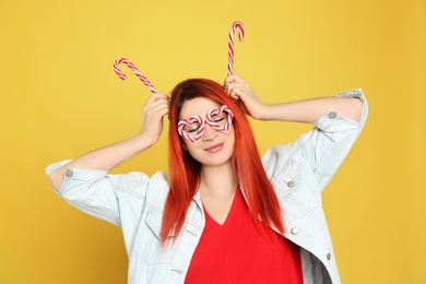 Young woman with bright dyed hair holding candy canes on yellow background