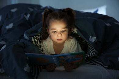 Photo of Beautiful little girl reading book in bed at night. Bedtime story
