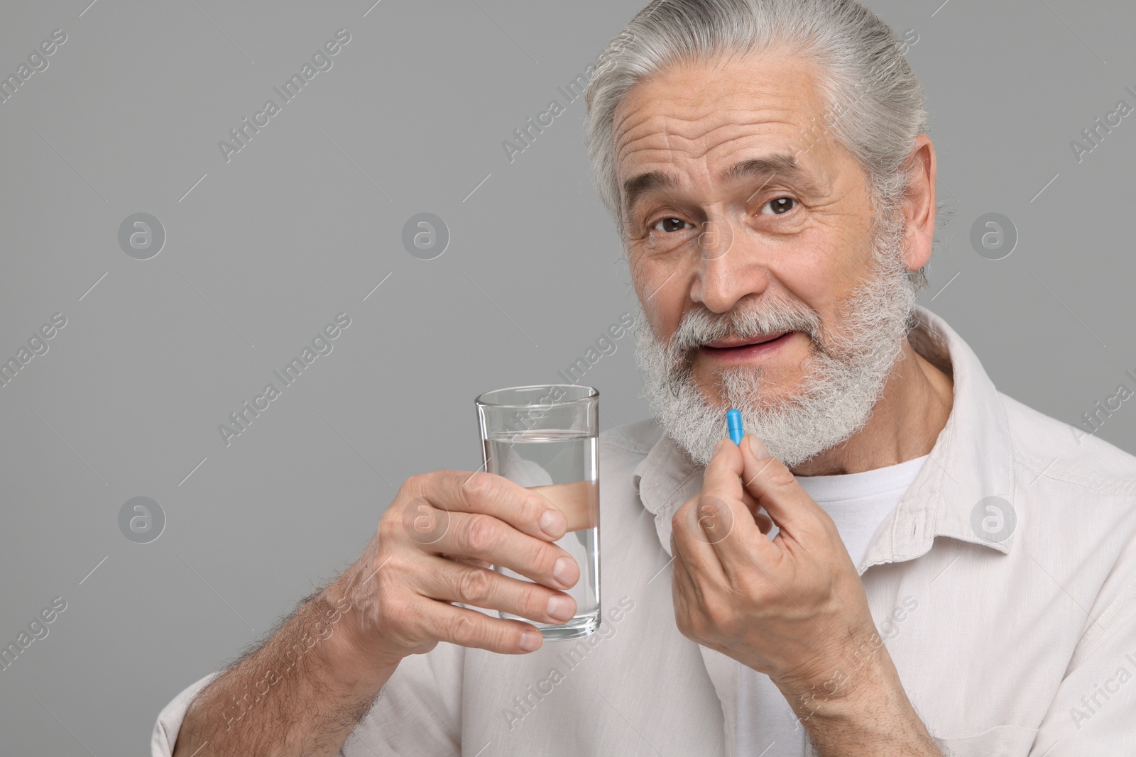 Photo of Senior man with glass of water taking pill on grey background