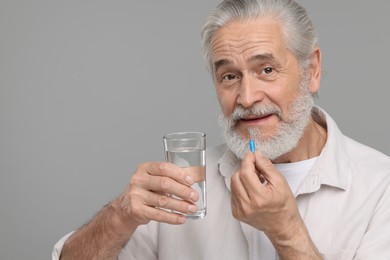 Photo of Senior man with glass of water taking pill on grey background