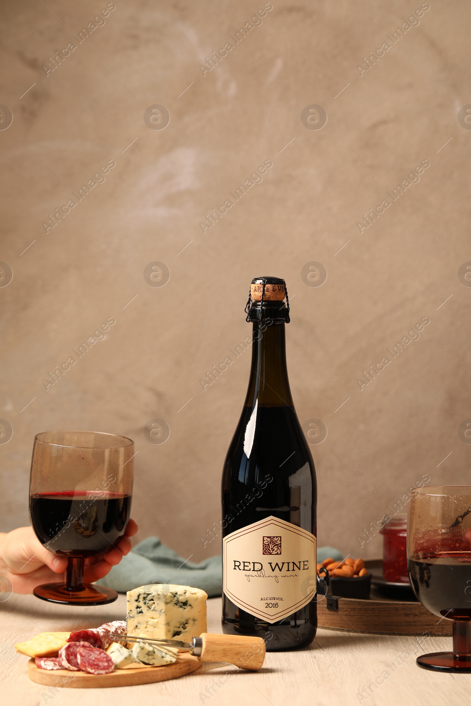 Photo of Woman holding glass of red wine at table with different snacks, closeup