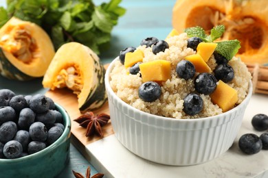 Photo of Tasty quinoa porridge with blueberries and pumpkin in bowl on table, closeup