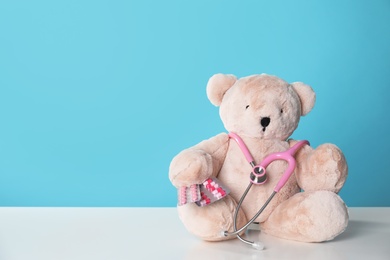 Toy bear with stethoscope and pills on table against color background, space for text. Children's hospital