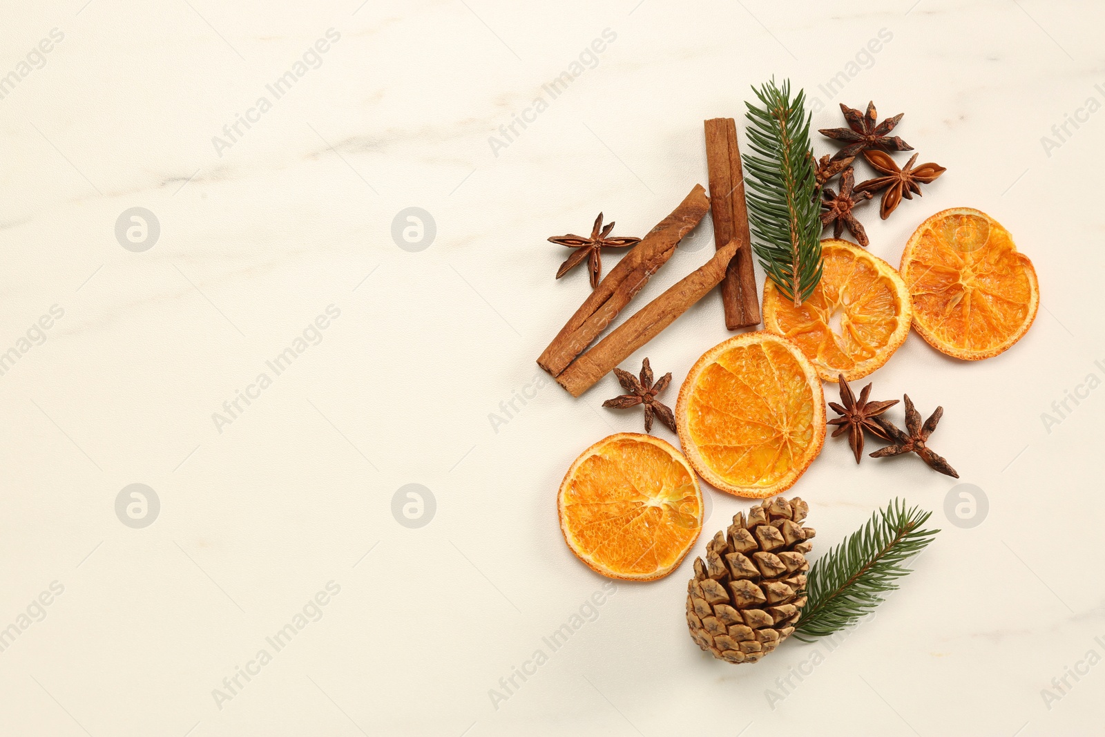 Photo of Dry orange slices, cinnamon sticks, fir branches and anise stars on white marble table, flat lay with space for text