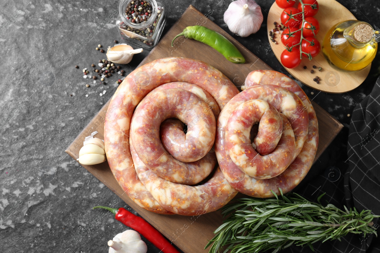 Photo of Raw homemade sausage, spices and other products on grey textured table, flat lay