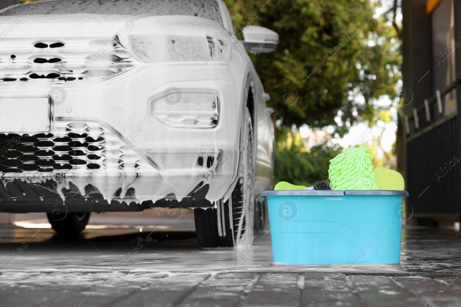 Photo of Auto covered with foam and cleaning products in bucket at outdoor car wash